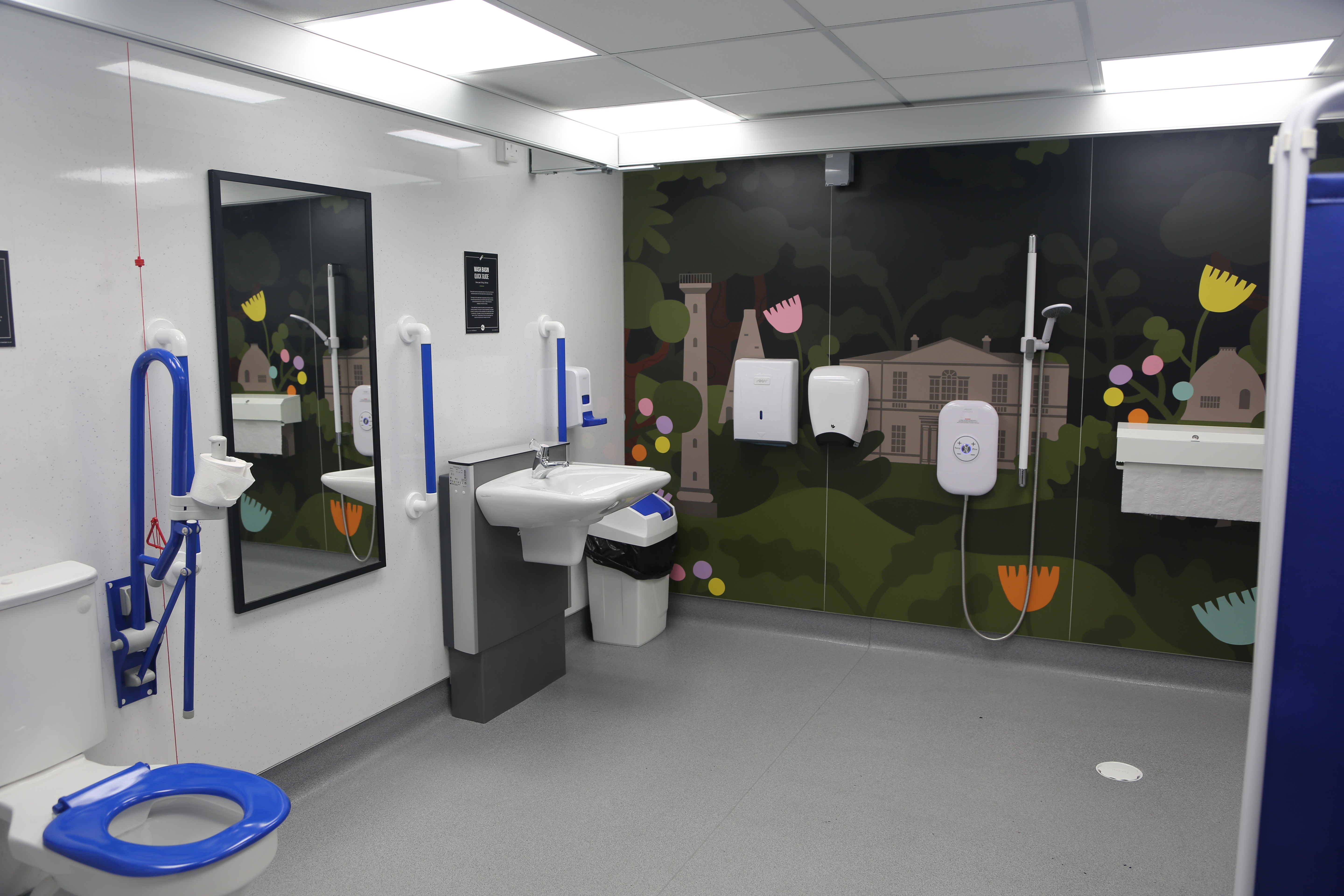 A Changing Places toilet at Clifton Park, with a toilet, sink and shower and a mural of the park