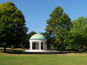 Clifton Park bandstand with grass in front of it, trees behind, and a clear blue sky