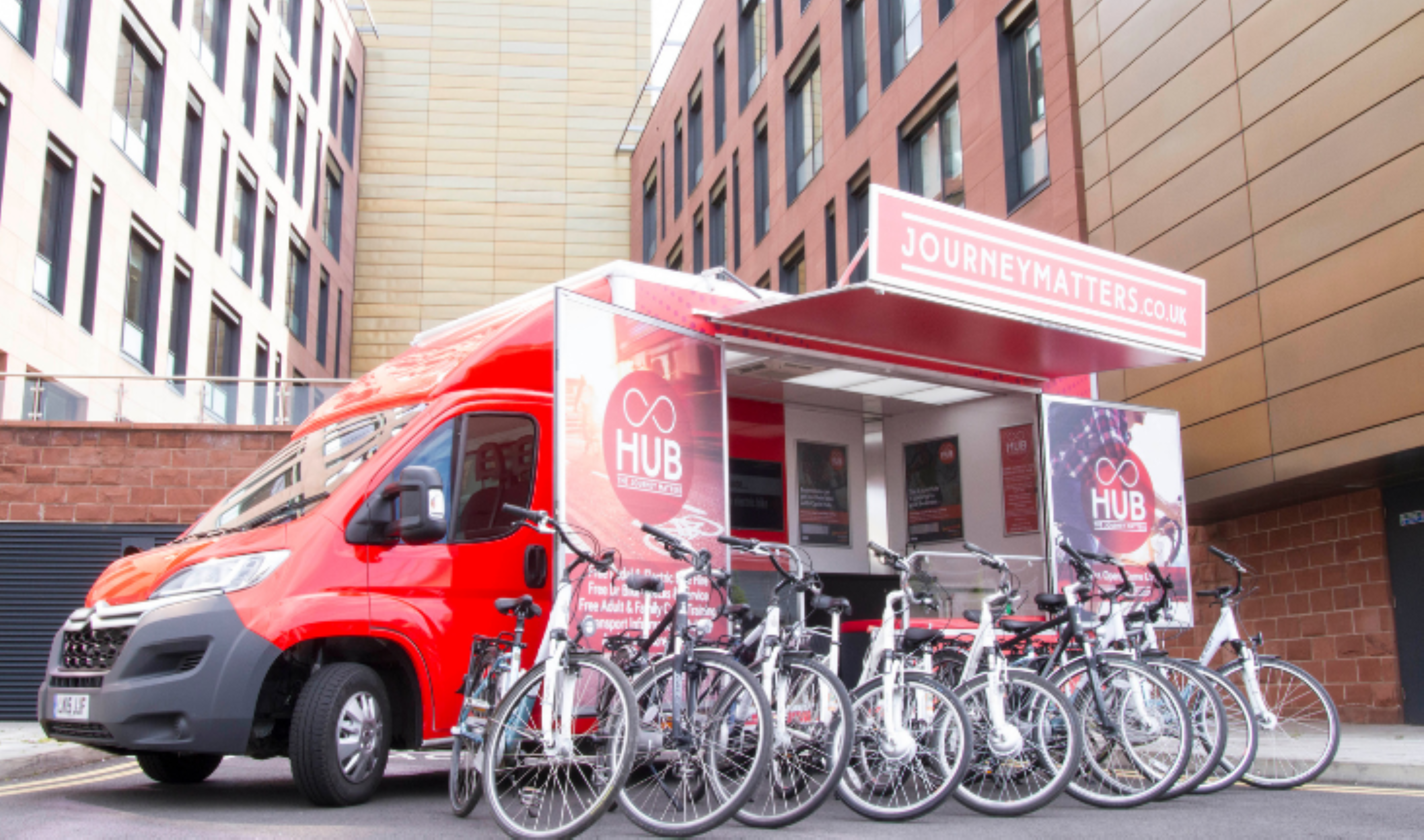 Red van with bikes in front of it with beige buildings in the background.