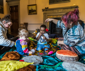 Two adults and two young children playing with autumn craft materials on the floor