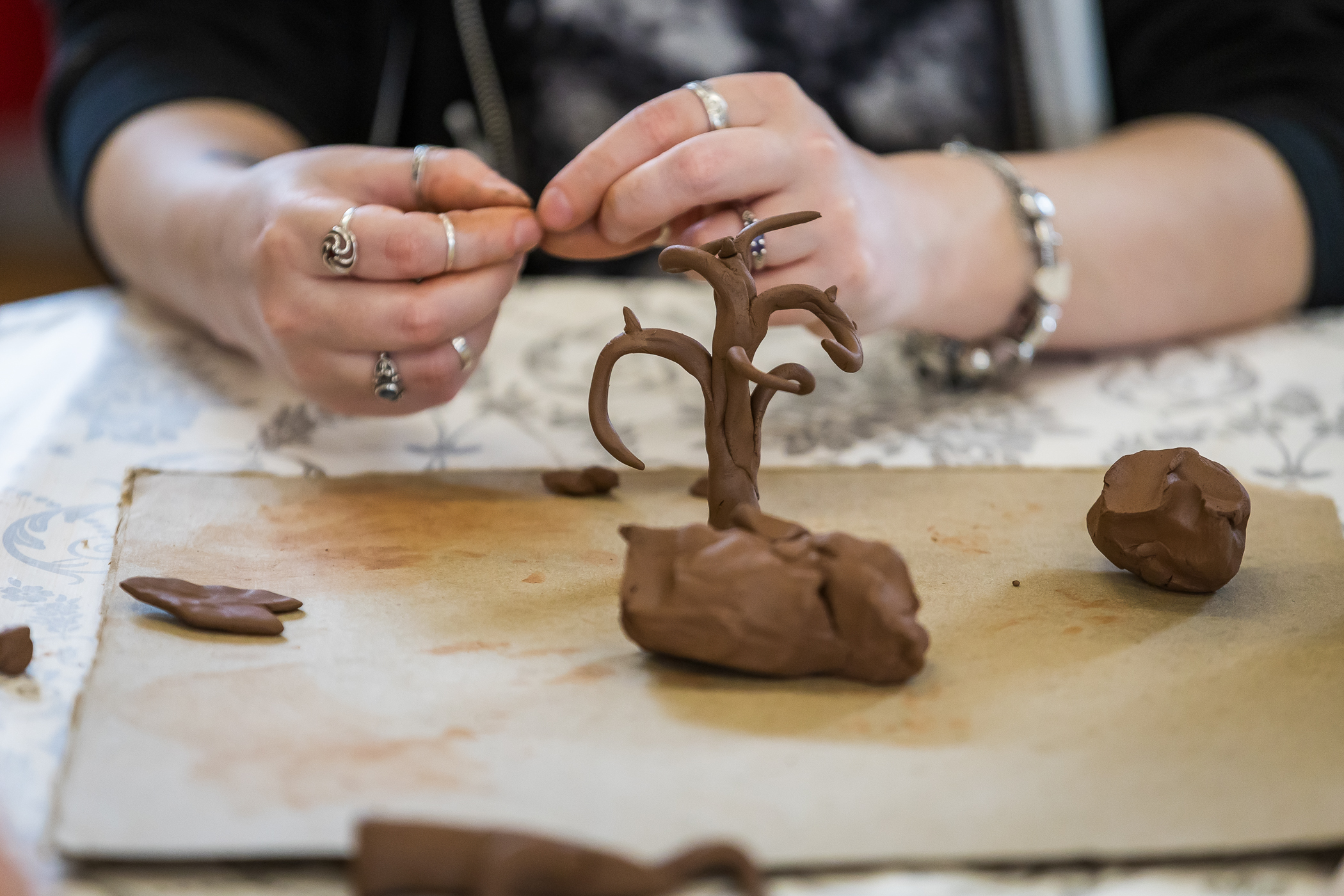 Woman creating a clay figure with brown clay on a work surface